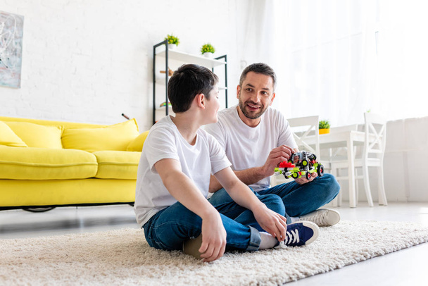 happy father and son sitting on carpet and playing with toy car at home - Fotoğraf, Görsel