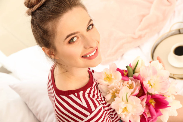 Young woman with bouquet of beautiful tulips sitting on bed - Foto, Imagem