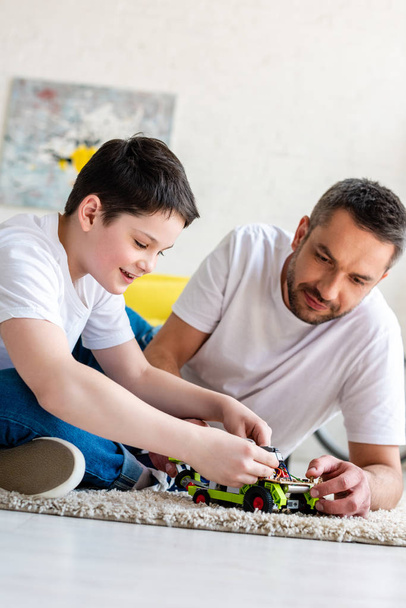 Vater und Sohn sitzen auf Teppich und spielen zu Hause im Wohnzimmer mit Spielzeugauto - Foto, Bild