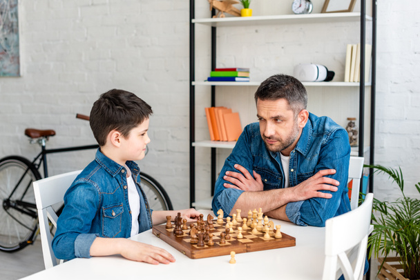 батько і син в денімі грають в шахи, сидячи за столом вдома
 - Фото, зображення