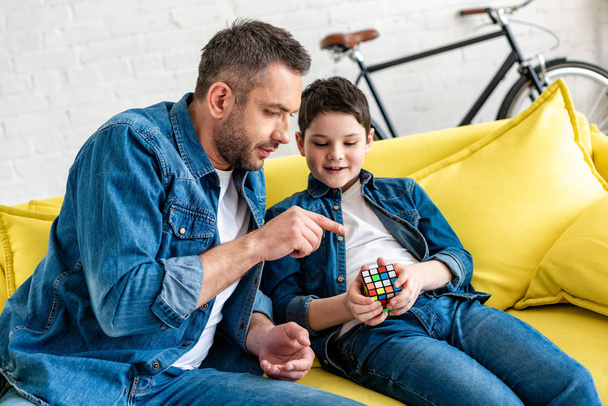 père assis sur le canapé avec son fils et pointant du doigt le cube jouet
 - Photo, image