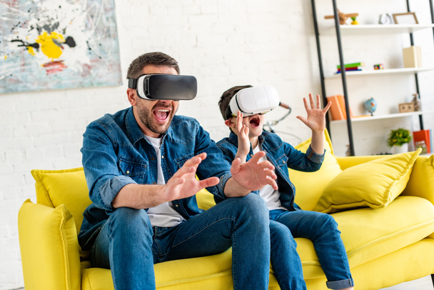 excited father and son in vr headsets experiencing Virtual reality on couch at home - Foto, imagen