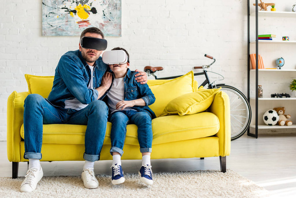 испуганный отец и сын в наушниках, испытывающих виртуальную реальность на диване дома
 - Фото, изображение