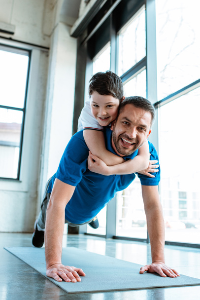 happy father doing push up exercise with son on back at gym - Photo, Image