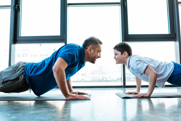 father and son looking at each other while doing push up exercise at gym - Foto, afbeelding