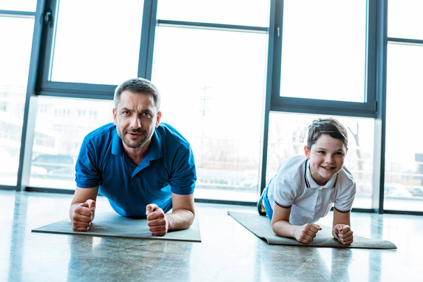 Vater und Sohn beim Plankentraining auf Fitnessmatten im Fitnessstudio - Foto, Bild