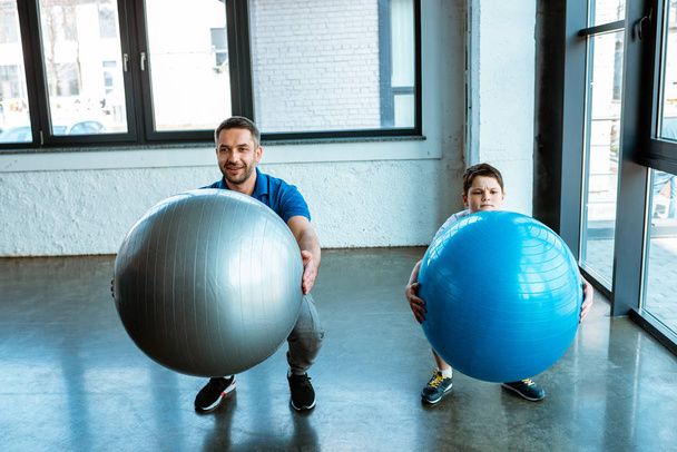 father and son doing squats with fitness balls at gym - Foto, Imagen