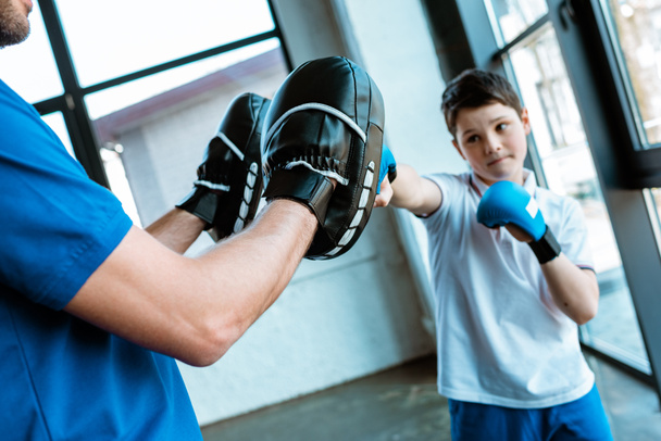 Junge in Boxhandschuhen trainiert mit Trainer im Fitnessstudio - Foto, Bild