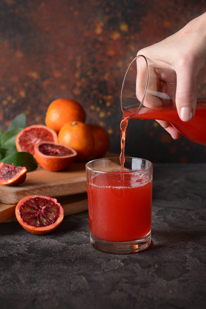 Femme verser du jus d'orange frais de sang de cruche dans le verre sur la table
 - Photo, image