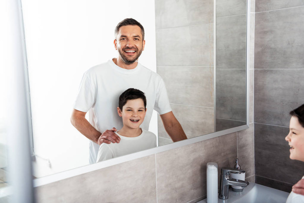 padre mirando a la cámara y abrazando sonriente hijo en el baño durante la rutina de la mañana
 - Foto, imagen