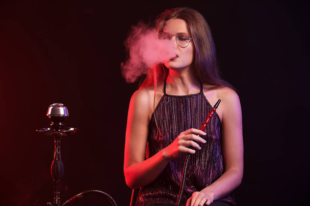 Young woman smoking hookah on dark background - Fotoğraf, Görsel
