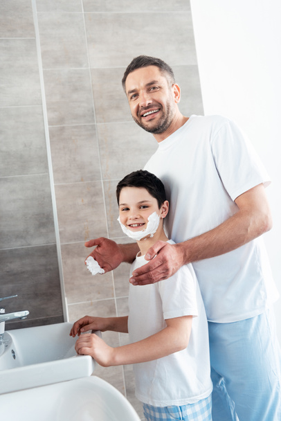 smiling father near son with shaving cream on face in bathroom - Photo, Image