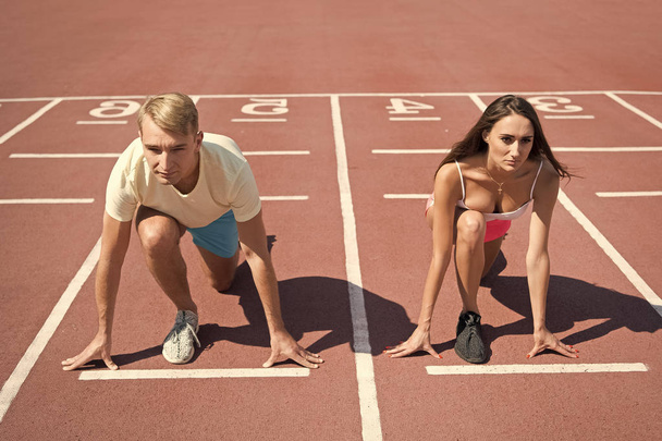 Equal forces concept. Man and woman low start position running surface stadium. Running competition or gender race. Faster sportsman achieve victory. Sport challenge for couples. Everyone has chance - Photo, image