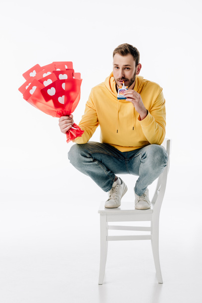 smiling man with bouquet of red paper cut cards with hearts symbols holding cigarette pack with instagram logo on white background - Photo, Image