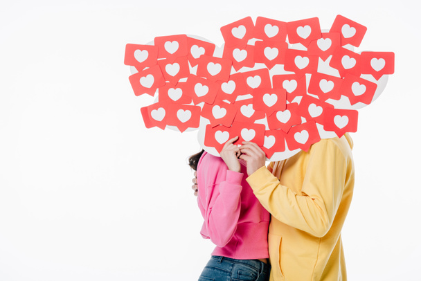 Молодой человек и женщина в ярких толстовках прячутся за лицами за красной бумагой разрезанные карточки с символами сердца изолированы на белом
 - Фото, изображение