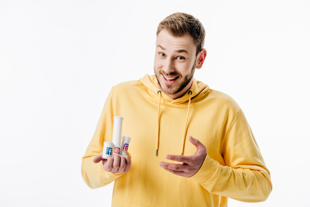 excited young man in yellow hoodie holding containers with social media logos isolated on white - Fotoğraf, Görsel