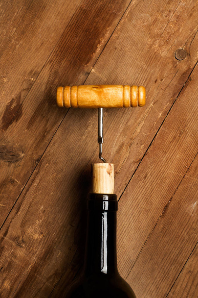 A corkscrew on a red wine bottle on a wooden table - Photo, Image