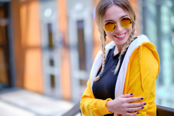 Beautiful  woman in a yellow sweatshirt and sunglasses on the st - Фото, изображение