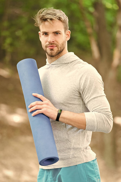 Practice yoga in park. Athlete always stretching after workout. Sportsman carries fitness mat for outdoor training. Outdoor yoga concept. Man athlete confident face carries mat going to stretching - Foto, imagen