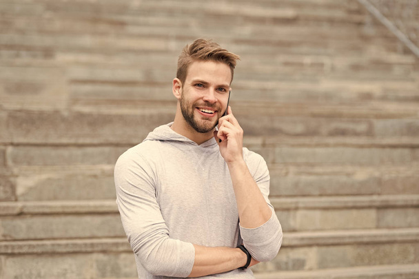 Keep in touch. Man bearded walks with smartphone, urban background with stairs. Man pleasant smiling face speaks on smartphone. Guy pleased answer call on smartphone. Pleasant conversation - Foto, Imagen