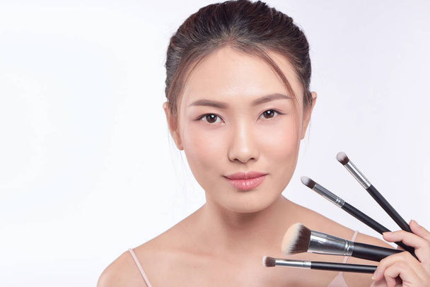 Portret van aantrekkelijke Aziatische lachende vrouw brunette geïsoleerd op witte studio opname met borstels voor make-up - Foto, afbeelding