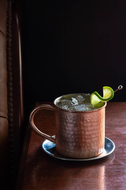 Cold Moscow Mule Cocktail in Copper Mug with Crushed Ice and Lime Garnish in Dark Luxurious Bar - Fotó, kép