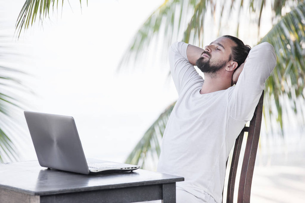 Vacation and technology. Work and travel. Young bearded man using laptop computer while sitting at beach cafe bar. - Foto, Bild