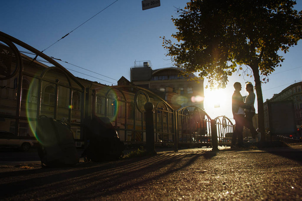 ευτυχισμένο ζευγάρι αγκαλιάζει στο δρόμο, οι ακτίνες ήλιων λάμπουν στα πρόσωπά τους, σκοτεινό φόντο. ημερομηνία στην πόλη - Φωτογραφία, εικόνα