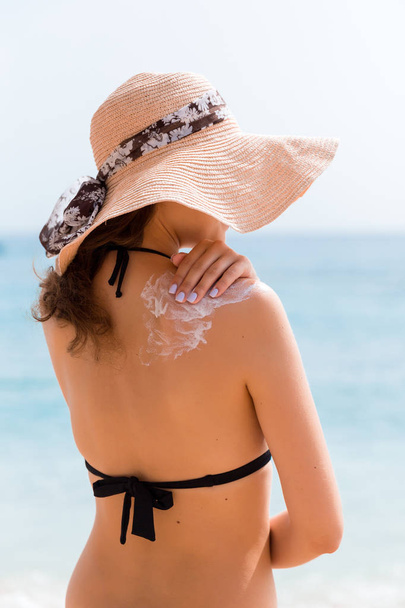 Красива жінка в капелюсі кладе сонячний крем на її плече на пляжі
 - Фото, зображення