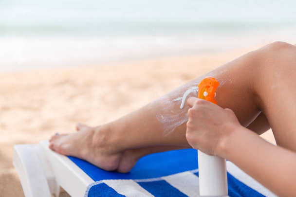 Девушка использует спрей для нанесения солнцезащитного крема на ногу на пляже
 - Фото, изображение
