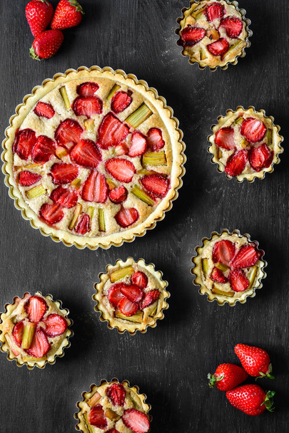 Homemade tarts with strawberry and rhubarb on black wooden background. Top view. Rustic style - Zdjęcie, obraz