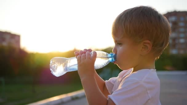 дитина п'є воду з пляшки на відкритому повітрі. Час заходу сонця
 - Кадри, відео