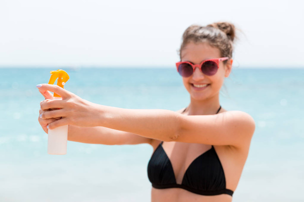 Young woman is holding a bottle of sunblock for body at the sea background - Photo, Image