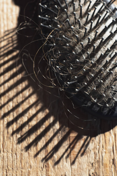 Black hairbrush with blonde hair on wooden floor. - Fotoğraf, Görsel