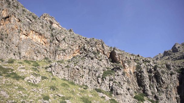 Вид знизу на скелястий гірський пік на тлі неба. Мистецтво. Мальовничі природні скелясті гори з нерівностями і виступами в чистий літній день
 - Фото, зображення