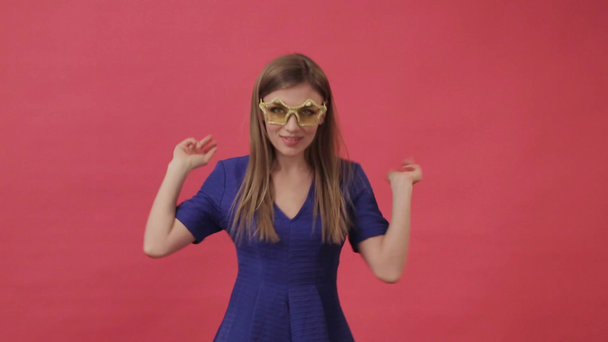 Beautiful girl in a dress dancing in yellow glasses in the form of a star. Studio, purple background - Materiał filmowy, wideo