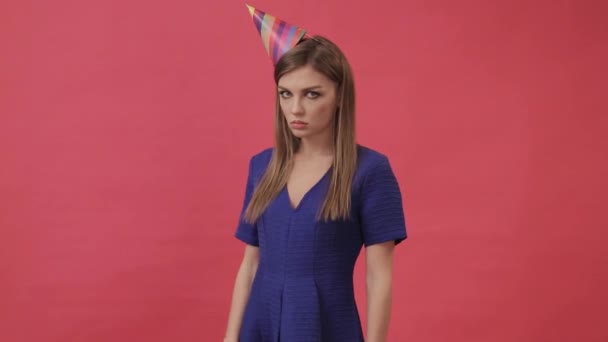 Sad girl in a festive hat, blowing a party whistle. Studio, purple background - Footage, Video
