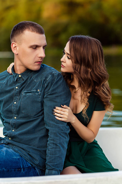 Young european couple is boating on a lake, young man and his girlfriend are sitting into boat at sunset, couple in love is boating on the river in the summer evening, happy couple on a romantic date - Foto, imagen