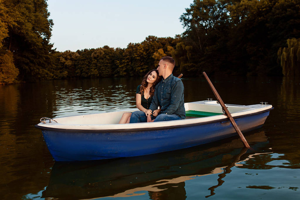 Young european couple is boating on a lake, young man and his girlfriend are sitting into boat at sunset, couple in love is boating on the river in the summer evening, happy couple on a romantic date - Zdjęcie, obraz