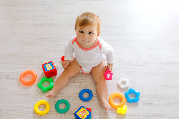 Adorable baby girl playing with educational toys in nursery. Happy healthy child having fun with colorful different toys at home. Kid trying to build plastic pyramid and using blocks with letters - Photo, Image