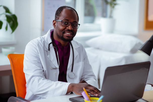 Afroamerický lékař, který sedí u stolu a pracuje na laptopu - Fotografie, Obrázek
