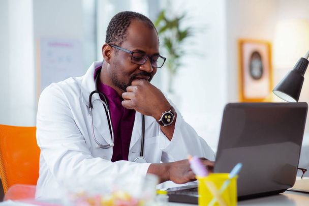 Dark-skinned doctor wearing glasses and watch feeling thoughtful - Photo, Image