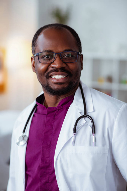 Handsome dark-skinned doctor smiling after good day at work - Фото, зображення