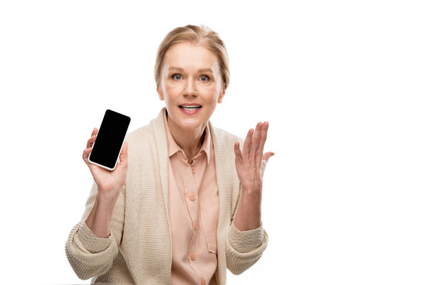 middelbare leeftijd vrouw Gesturing en het tonen van smartphone met blanco scherm geïsoleerd op wit - Foto, afbeelding