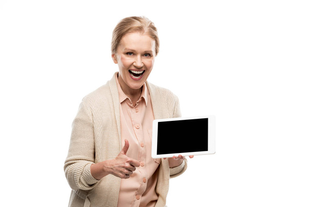 возбужденная женщина средних лет делает большой палец вверх знак и проведение цифровой планшет с пустым экраном изолированы на белом
 - Фото, изображение