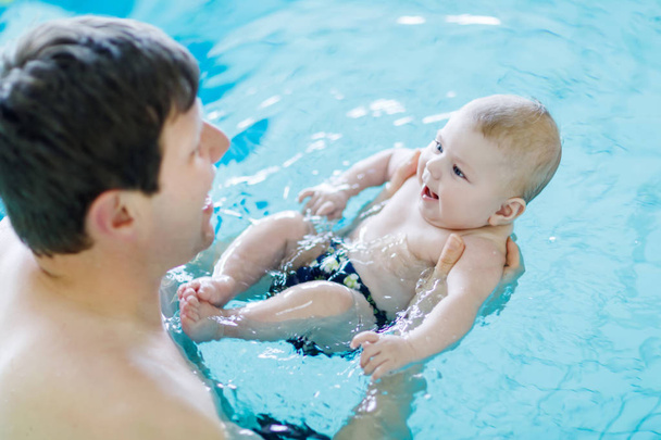 Happy middle-aged father swimming with cute adorable baby in swimming pool. - Photo, Image