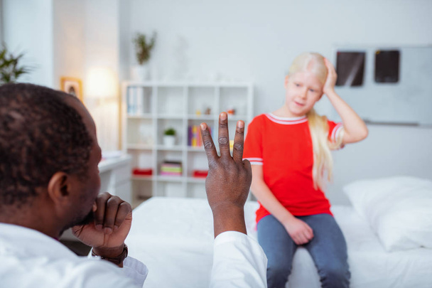 Dark-skinned doctor showing girl with concussion three fingers - Fotó, kép