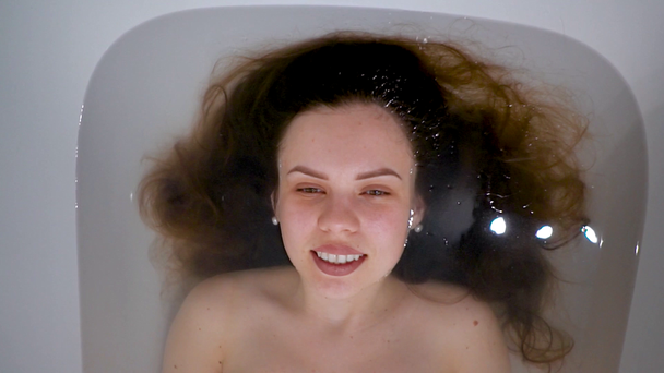 Gyönyörű lány feküdt a fürdőszobában nyitja meg szemét, és mosolyog - Felvétel, videó