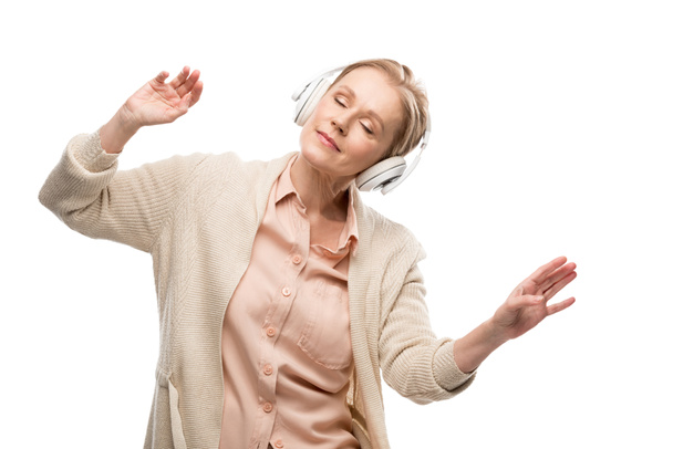 жінка середнього віку з закритими очима в навушниках прослуховування музики і жестами ізольований по білому - Фото, зображення