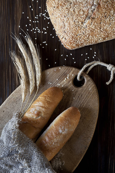 Loaf of wheat bread with sesame, ears of wheat and french bread  - Foto, afbeelding